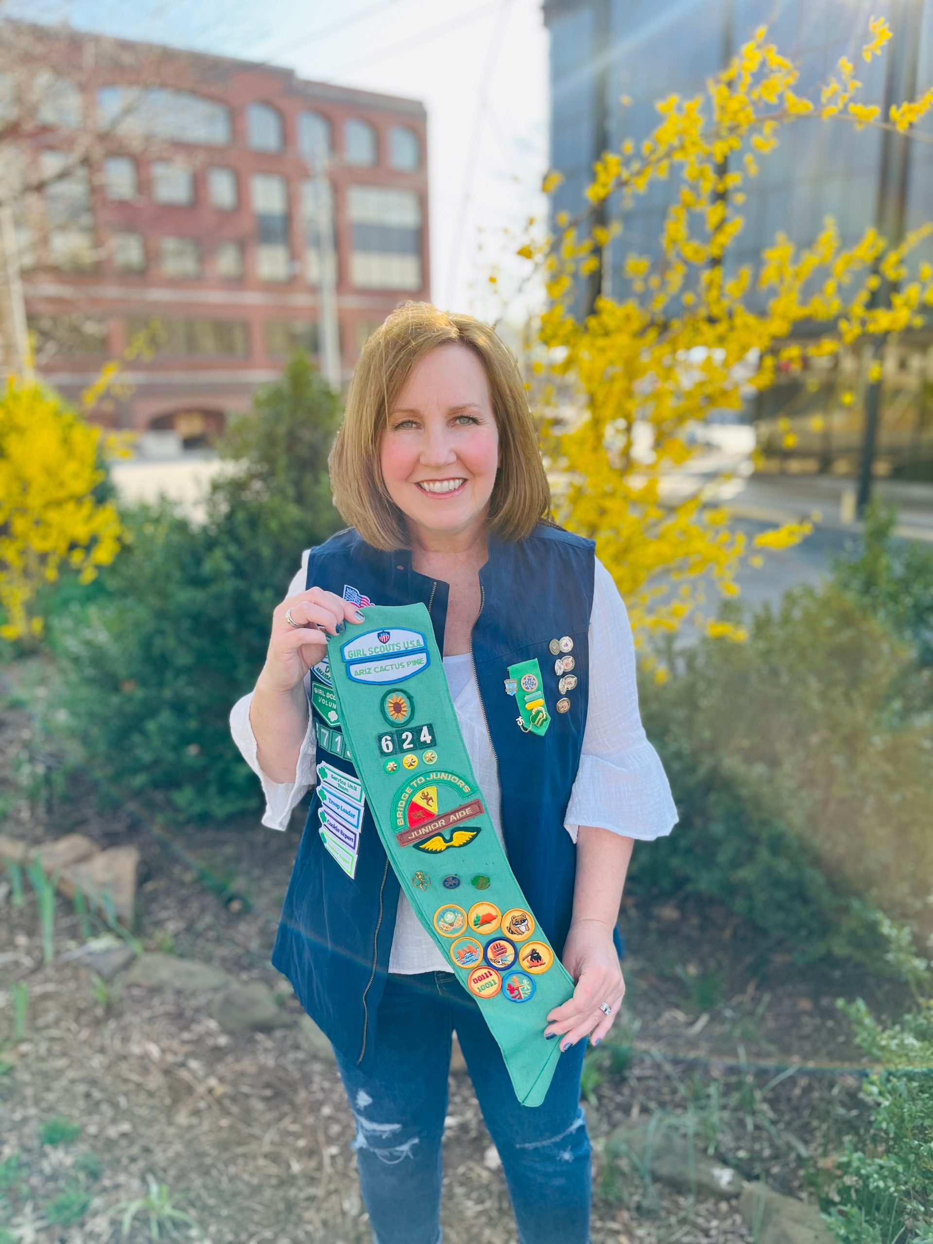 Adult Girl Scout and alumnae posing with Girl Scout sash full of Girl Scouting accomplishments