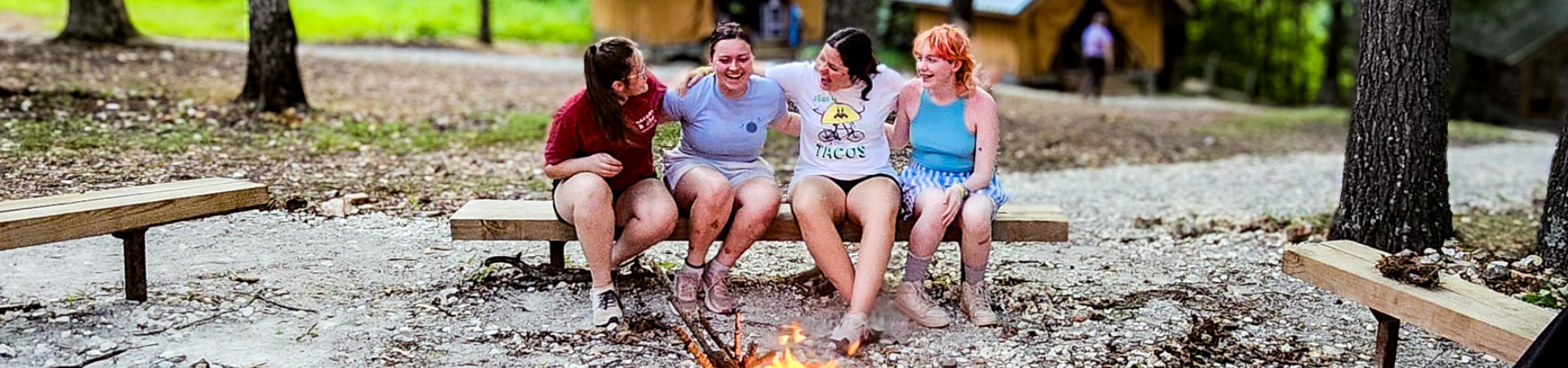  four older Girl Scouts sitting on a bench in front of a camp fire 