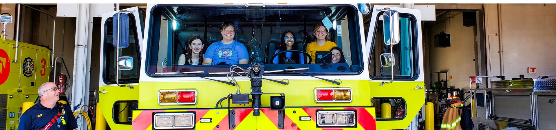  5 girls posing in the cab of a large fire truck 