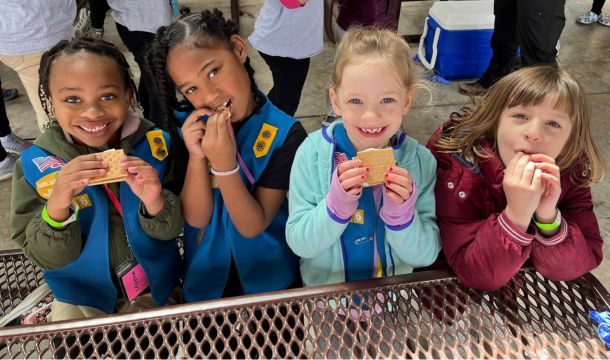 group of four daisy girl scouts at a picnic table enjoying s'mores
