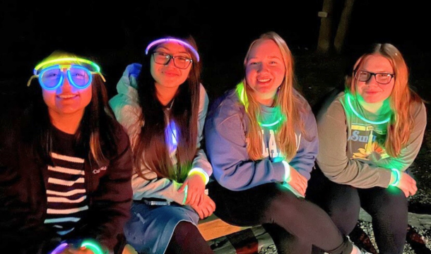 Older Girl Scouts sitting on a bench at night wearing glow-stick jewlery