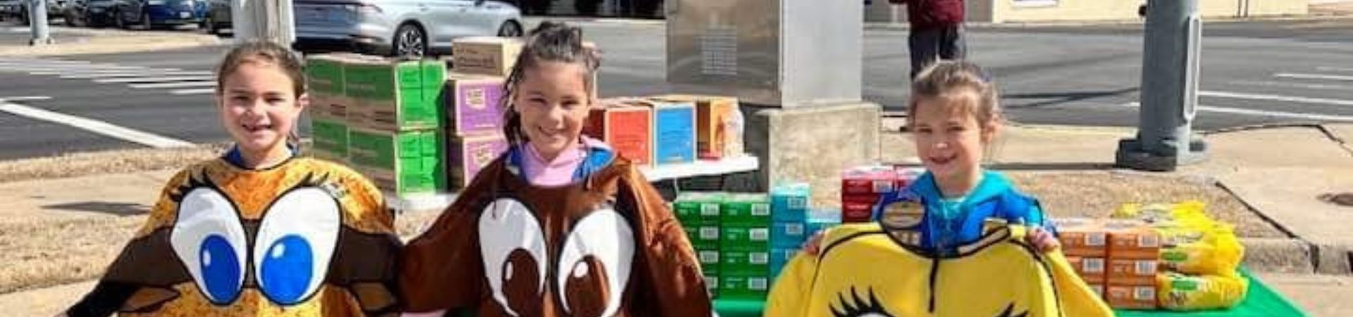  three girls at a Girl Scout cookie booth wearing cookie costumes 