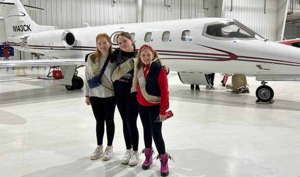 3 girls standing in front of an airplane in a hanger