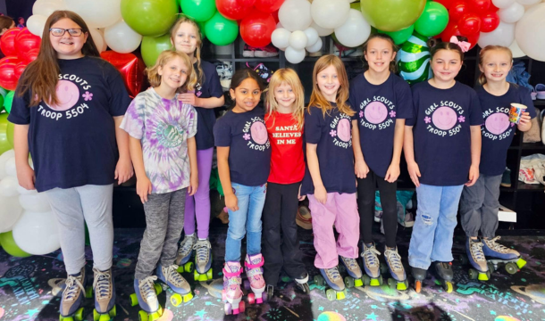 Large group of girls wearing roller skates and posing in front of a balloon wall