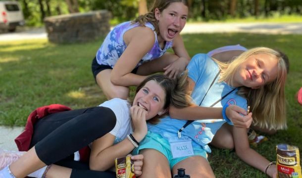 3 girls sitting very close on the ground laughing and eating snacks