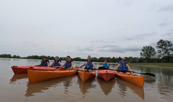 4 girls and 2 instructors in 5 kayaks on a lake