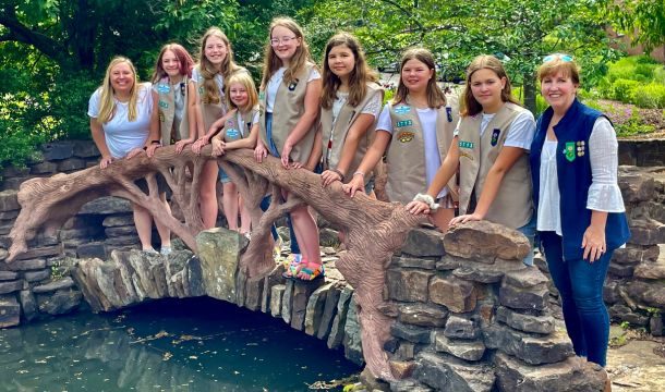 Girls in Girl Scout uniforms standing on a bridge with their Troop Leaders