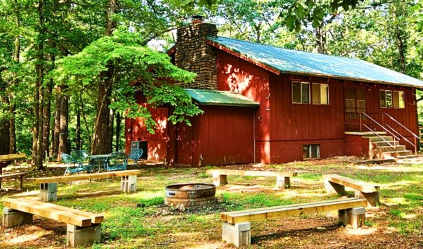 Red building with green roof and tall stone chimney with a firepit area in front