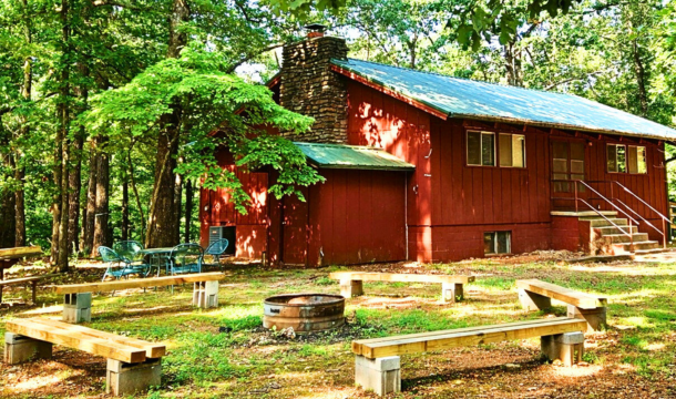 Red building with green roof and tall stone chimney with a firepit area in front