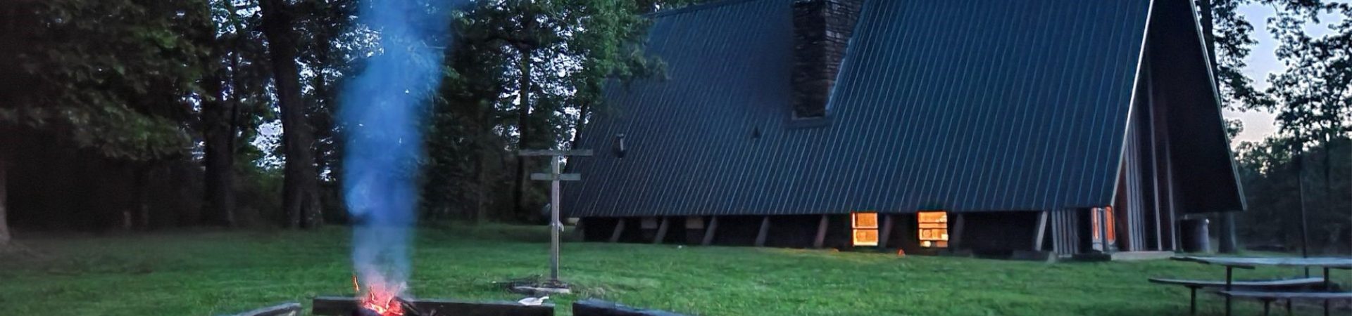  exterior of a frame chalet at dusk with campfire going in fire circle 