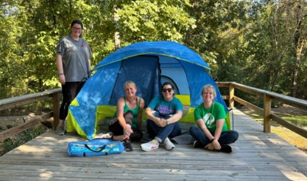 3 volunteers seated in front of a small tent