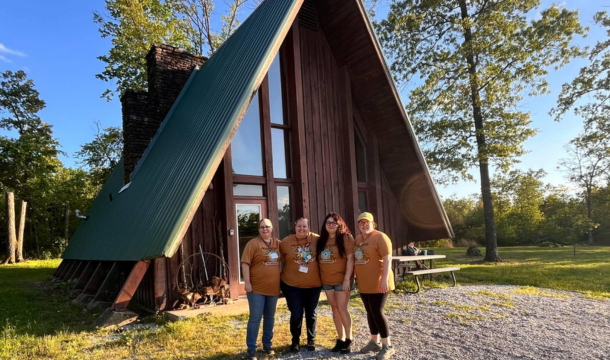 group of four adult volunteers in front of a camp building