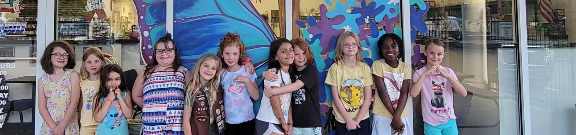  group of junior girl scouts walking outside hugging smiling at camera in junior vest and sash with badges 