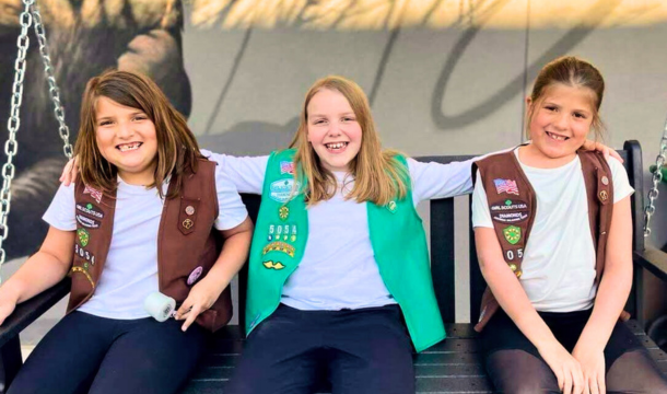 Two Brownie Girl Scouts and a Junior Girl Scout sitting on an outdoor swing smiling