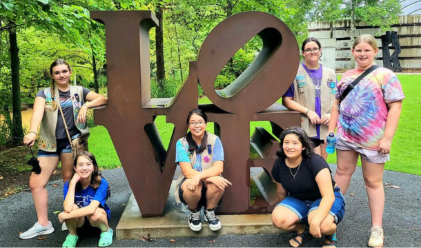 Six girl scouts posing around a large L-O-V-E sculpture