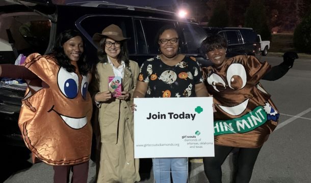 four adult women in girl scout themed halloween costumes with a join today sign