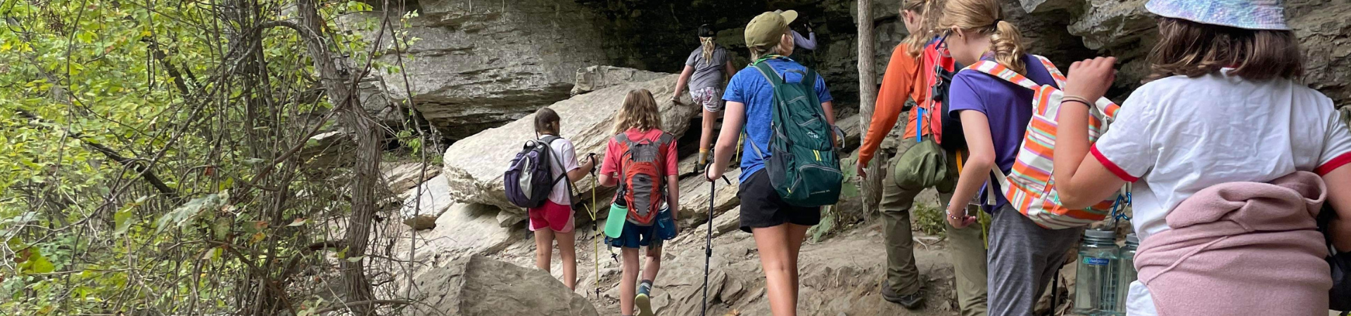  group of girls with backpacks hiking a trail by rock bluffs 