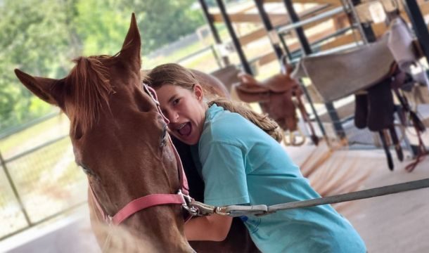 girl hugging a brown horse in a barn
