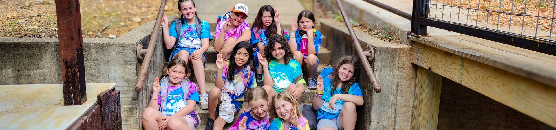  large group of girls in tie-dye summer camp t-shirts posed in front of Camp NOARK sign 