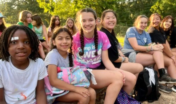 large group of campers and counselors sitting on bench smiling at camera