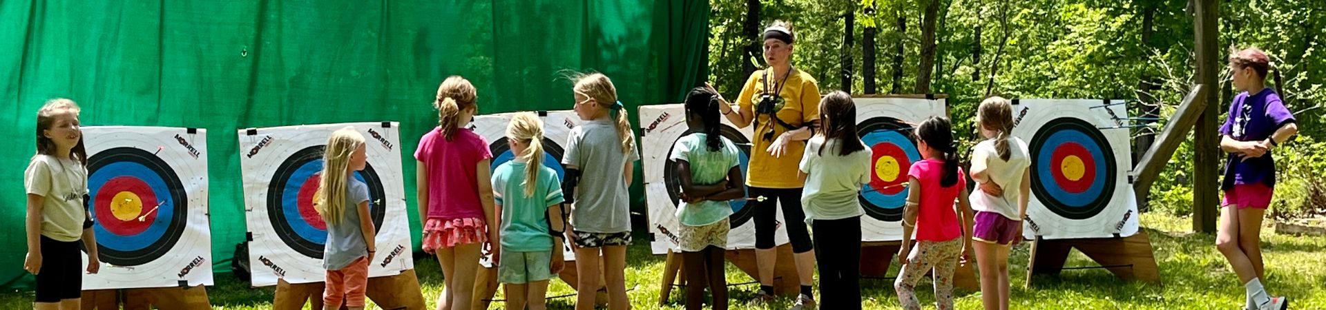  Row of girls from behind shooting bow and arrows at targets 