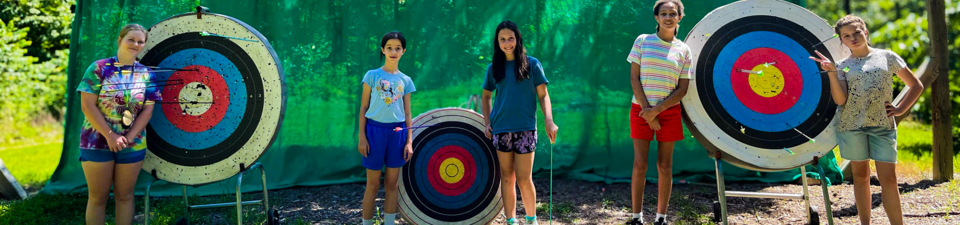  Row of girls from behind shooting bow and arrows at targets 