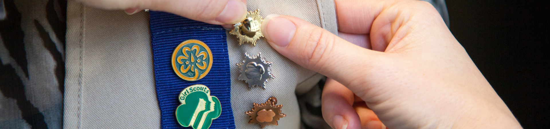  close up on uniform of a girl scout being pinned with a gold award pin, alongside her silver pin and bronze 