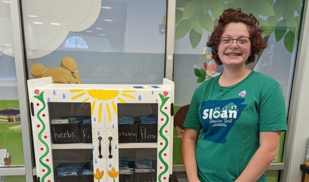 gold award girl scout standing next to a free garden seed box