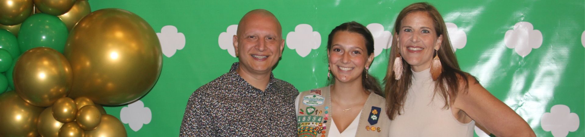  girl scout with adult male and female in front of photo backdrop 