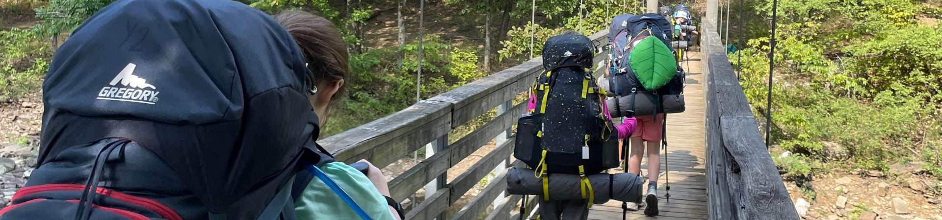  Group hiking away from camera across a bridge with a lot of backpacking gear 