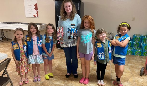 older girl volunteer standing in the middle of six daisy girl scouts