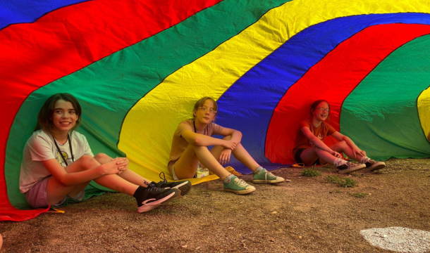 3 older Girl Scouts sitting under a colorful parachute